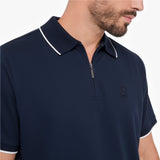 A close-up of a man wearing a navy blue polo shirt with a half-zip collar and white contrast piping on the collar and sleeve cuffs. The shirt features a small embroidered dog logo on the left chest.