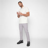 A man modeling a white short-sleeve polo shirt and light gray trousers with black sneakers, standing against a plain light gray studio background.