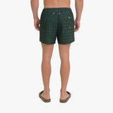 A man viewed from the back wearing dark green patterned swim trunks and olive green sandals