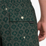 Close-up of a person wearing patterned green shorts with a palm tree and dog motif, a front-buttoned pocket, and a visible James Bark brand tab.