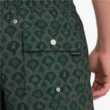 Close-up of a person wearing patterned green shorts with a palm tree and dog motif, a front-buttoned pocket, and a visible James Bark brand tab.
