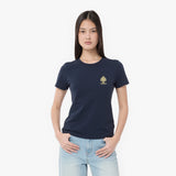 A woman modeling a navy blue T-shirt with a small gold spade logo on the left chest, paired with light blue jeans