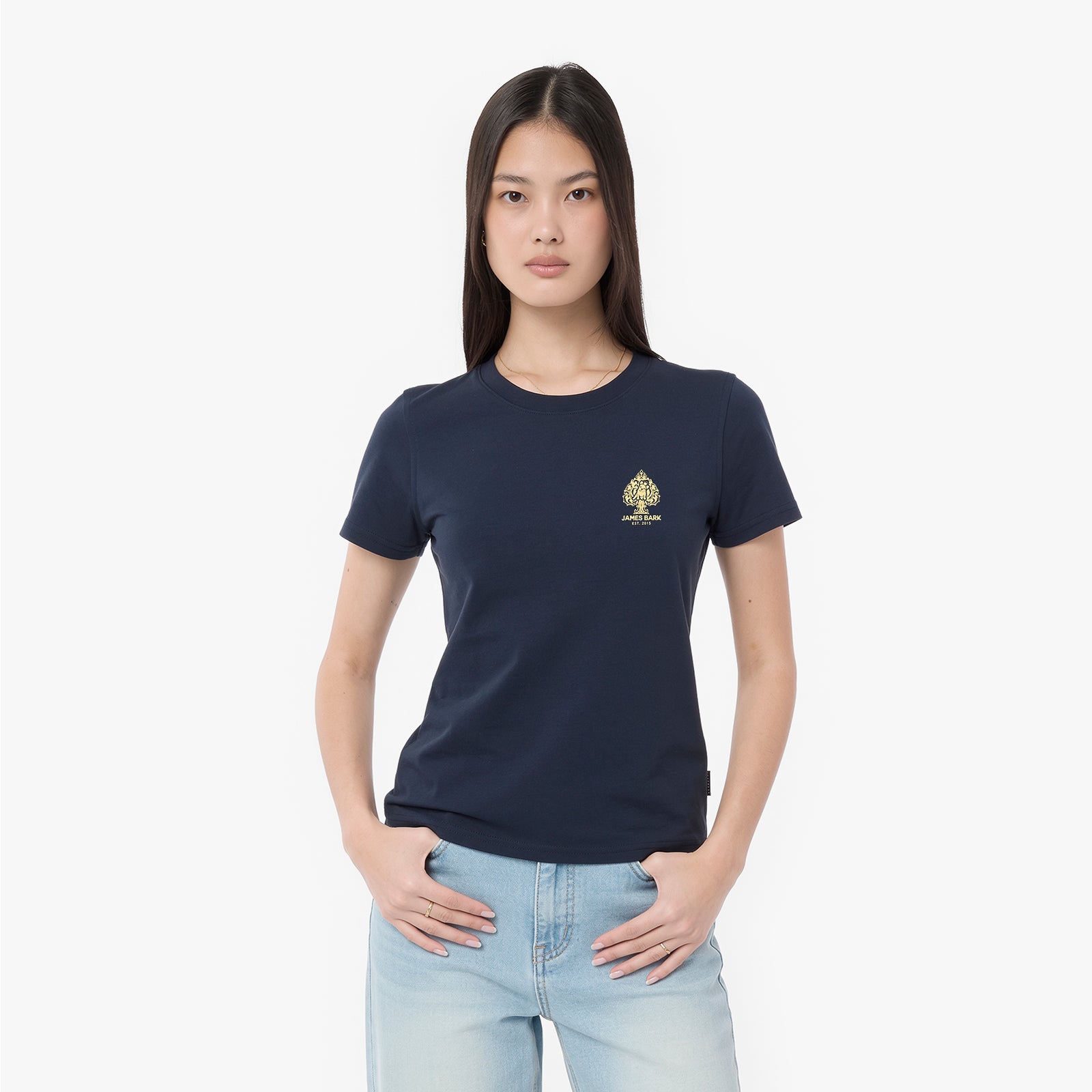 A woman modeling a navy blue T-shirt with a small gold spade logo on the left chest, paired with light blue jeans