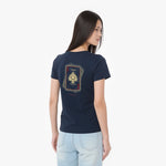 A woman shown from the back wearing a navy blue t-shirt with a gold and red playing card graphic on the back, paired with light blue jeans