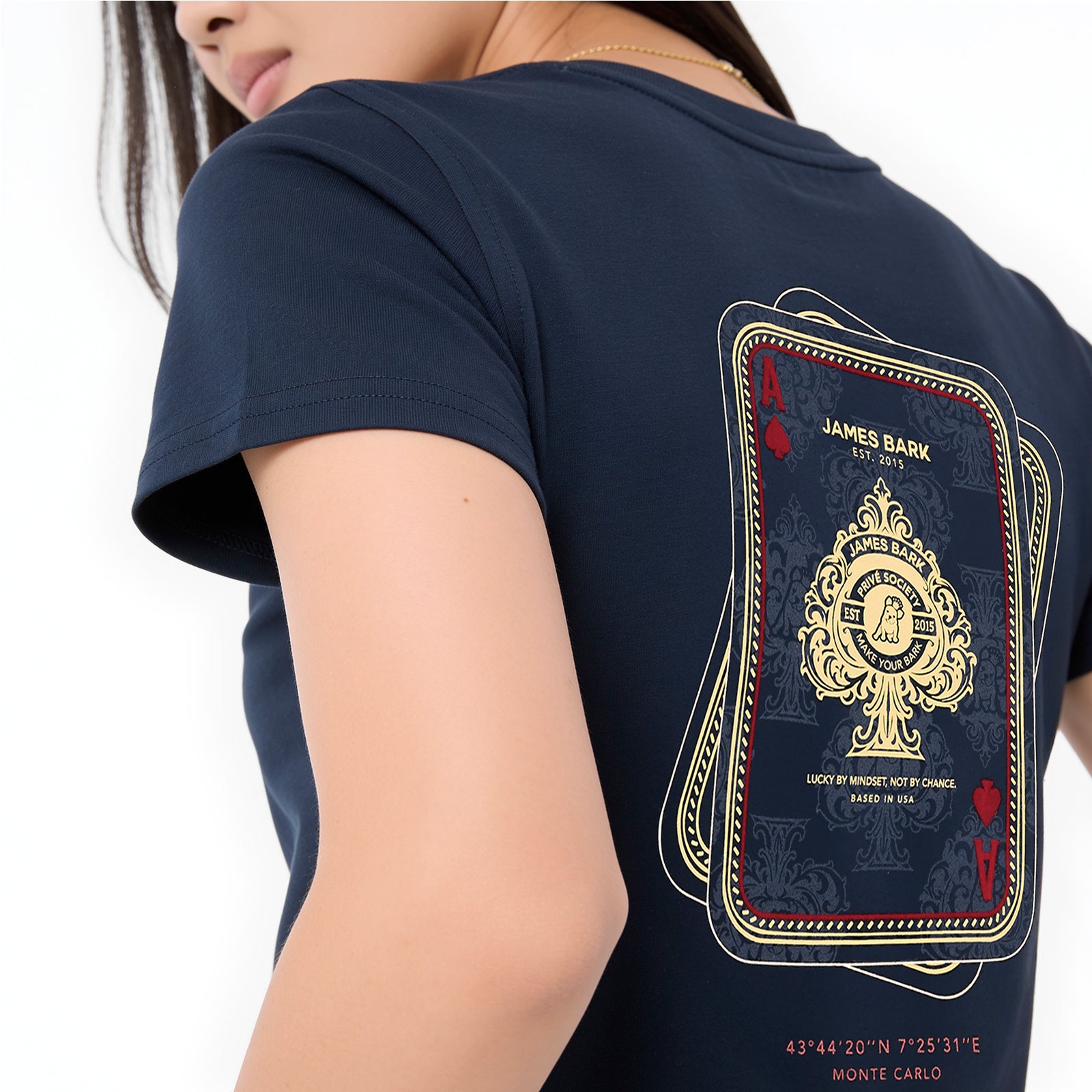 A close-up of a model wearing a navy blue t-shirt, showing the back graphic. The graphic is styled like a playing card deck with gold and red details, featuring the text 'JAMES BARK EST.