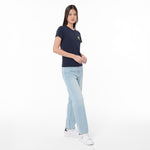 A woman modeling a navy blue T-shirt with a small yellow embroidered logo on the left chest, paired with light-wash blue jeans and white sneakers