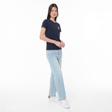 A woman modeling a navy blue T-shirt with a small yellow embroidered logo on the left chest, paired with light-wash blue jeans and white sneakers