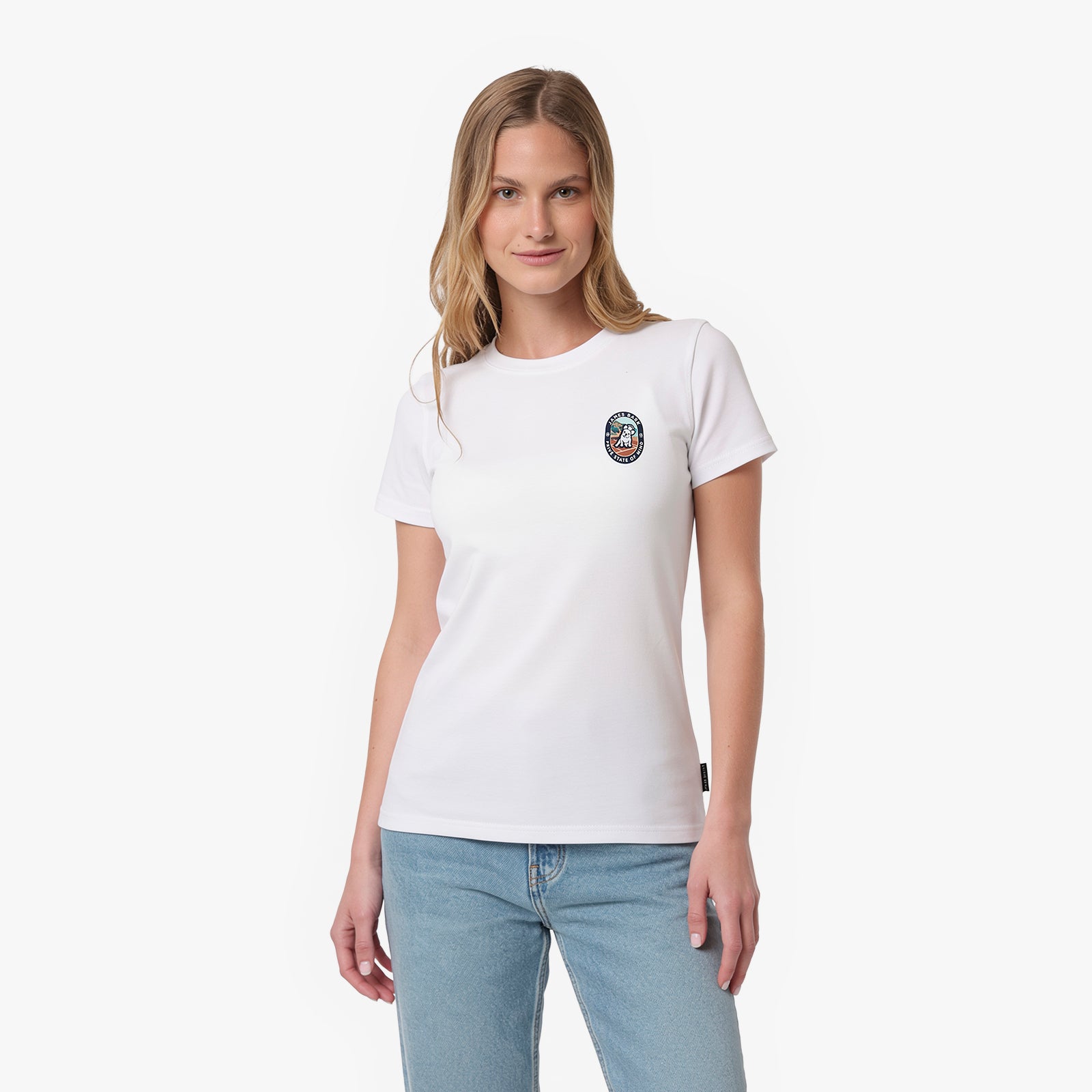 A woman modeling a white T-shirt with a small circular multicolor graphic on the left chest