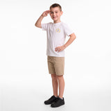 A young boy modeling a white short-sleeve t-shirt with a small gold crest on the left chest, paired with khaki shorts and black sneakers, standing against a plain white studio background.