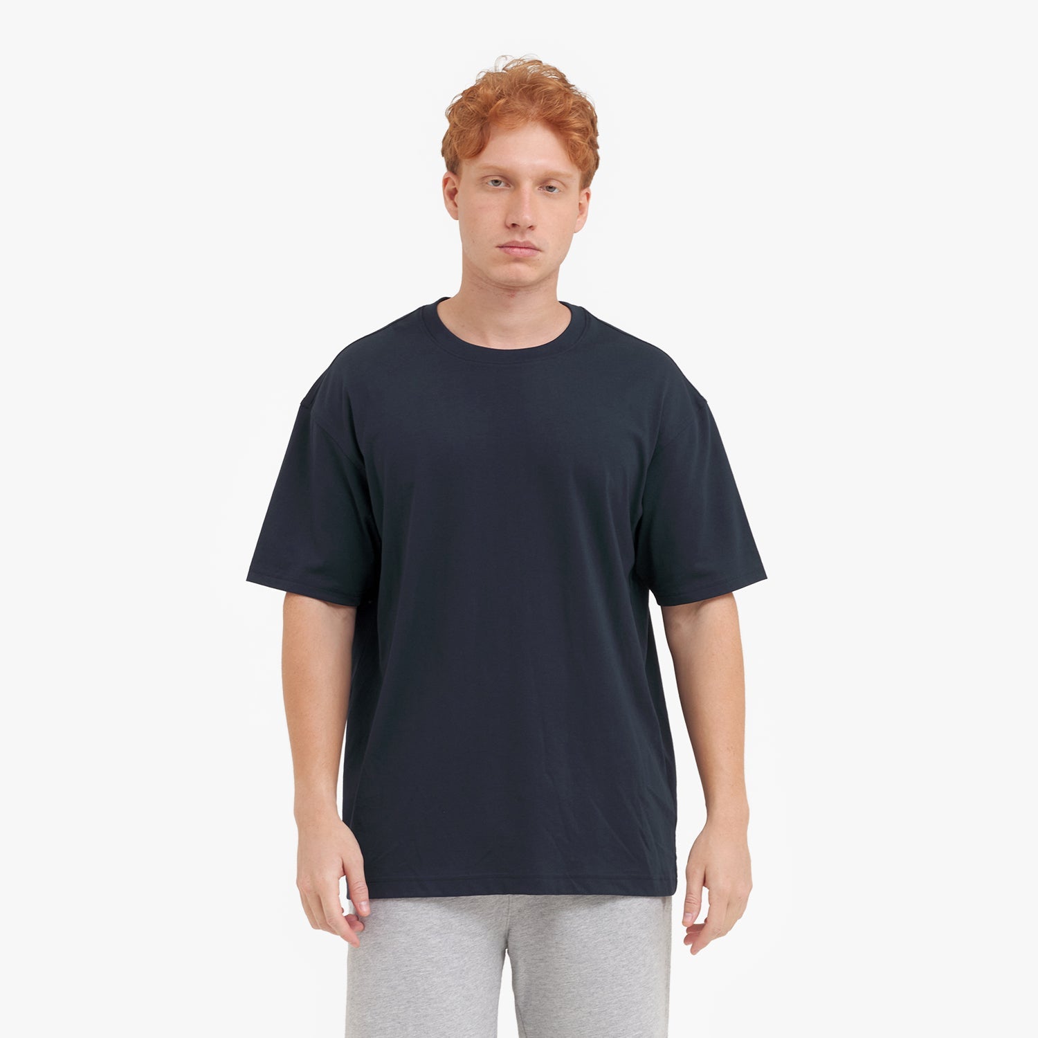 Man wearing a plain black t-shirt and light gray pants on a white background