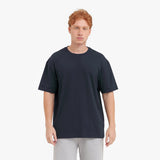 Man wearing a plain black t-shirt and light gray pants on a white background