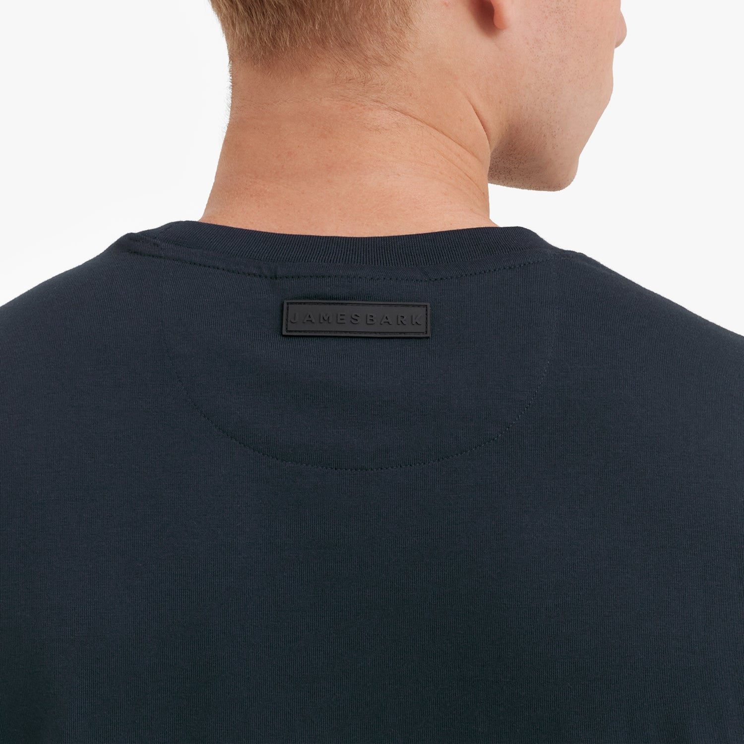 Close-up of a navy blue t-shirt with a brand label on the back against a white background