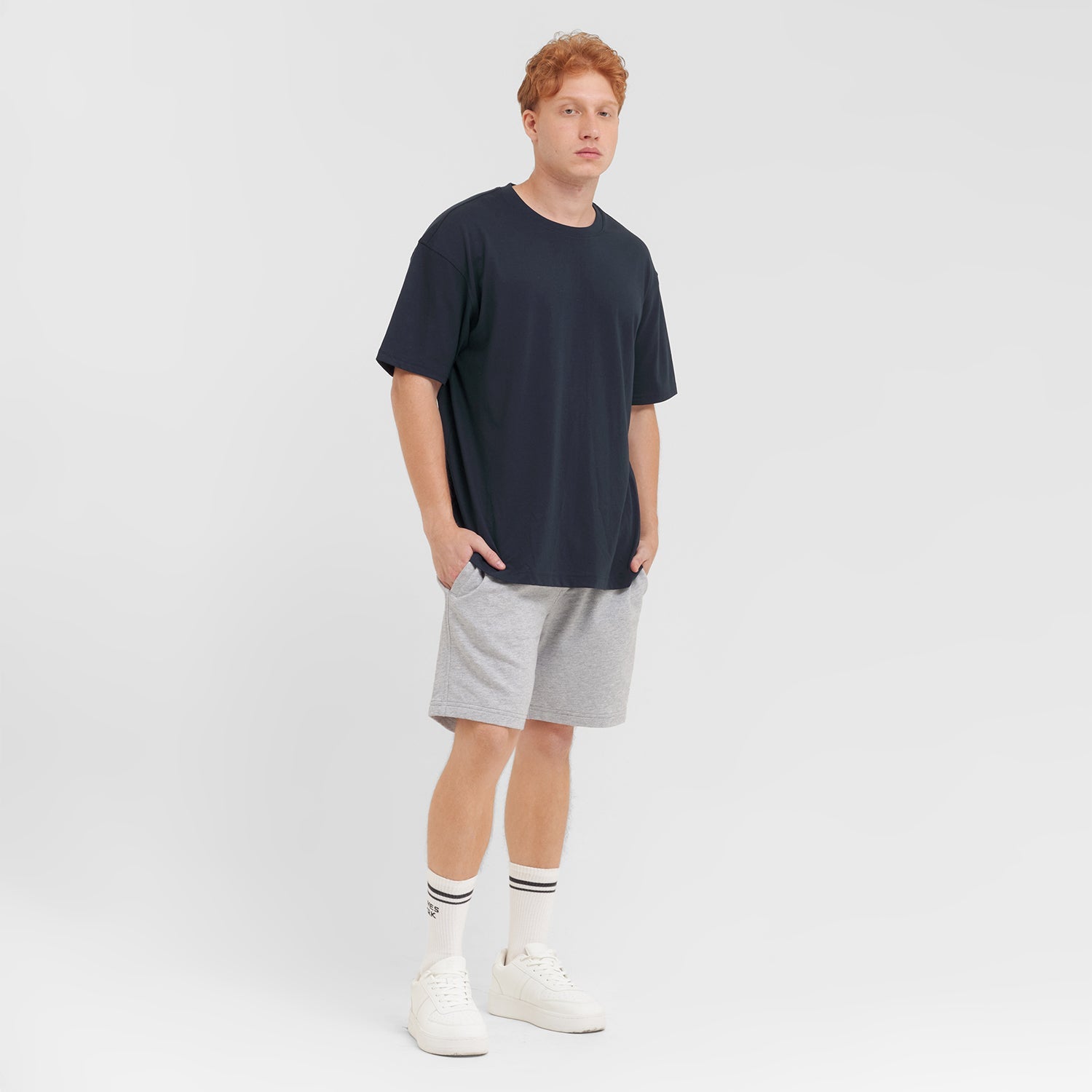 Man wearing a navy t-shirt, gray shorts, and white sneakers on a light gray background