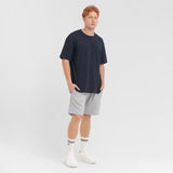 Man wearing a navy t-shirt, gray shorts, and white sneakers on a light gray background