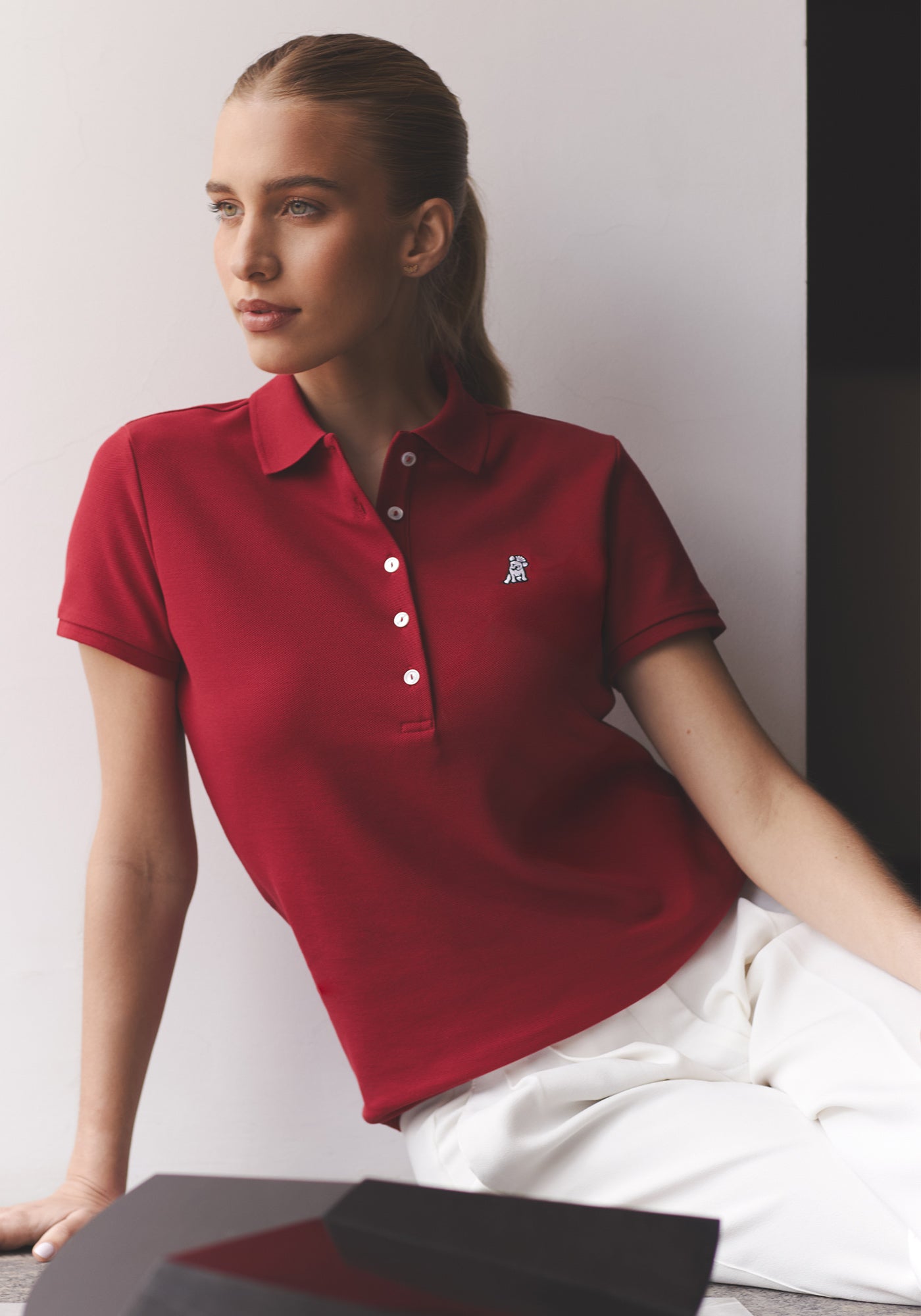 Una mujer con cola de caballo, vistiendo un polo rojo y pantalones blancos