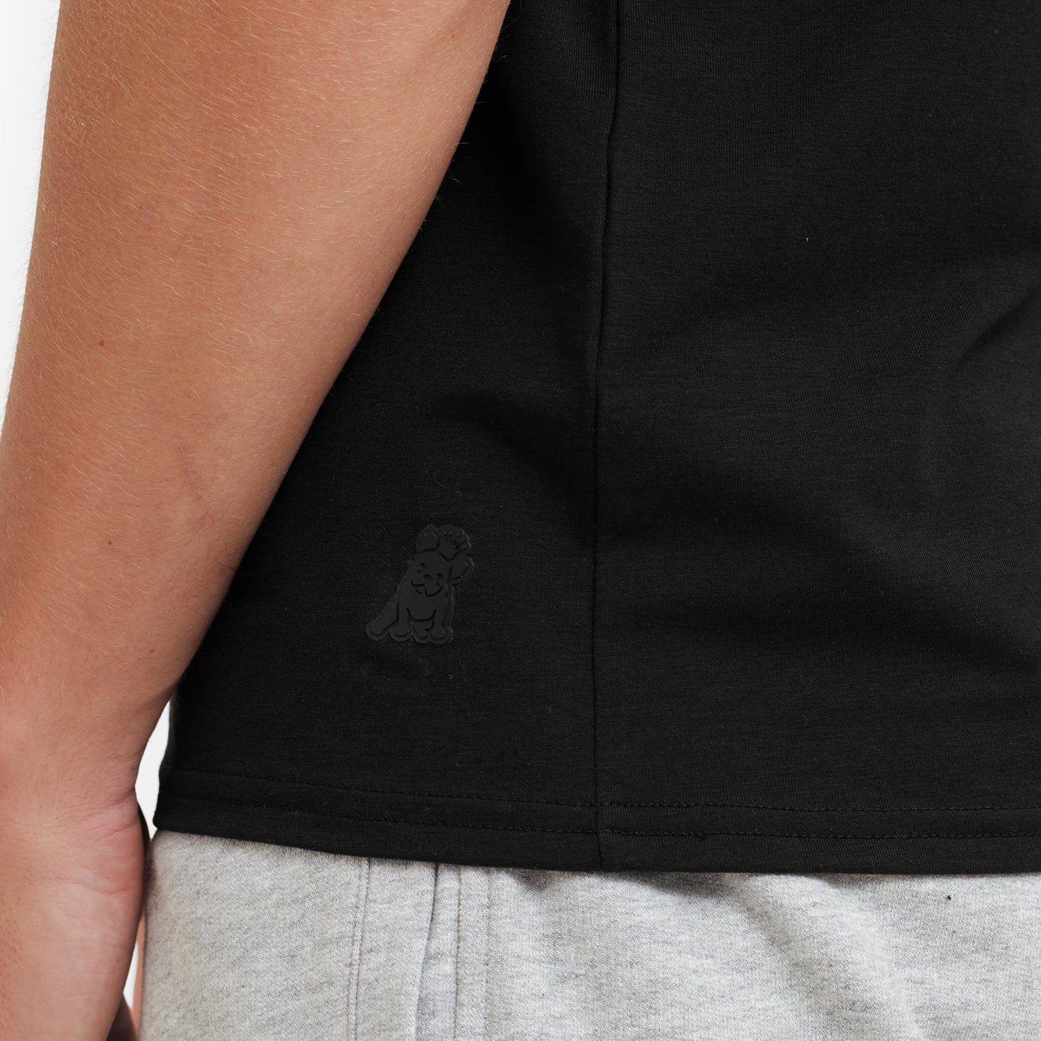 Black t-shirt with a logo on the chest worn by a person, with gray shorts visible.