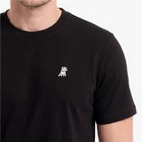 A close-up of a man wearing a black short-sleeve crewneck t-shirt with a small white embroidered dog 