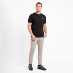 A man modeling a black short-sleeve crewneck t-shirt with a small white logo on the left chest, paired with beige trousers