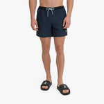 A man wearing dark navy blue swim shorts with a black waistband and a white drawstring, paired with black slide sandals