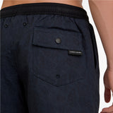 Close-up of a man wearing dark navy blue swim shorts with a black waistband and a JAMES BARK label