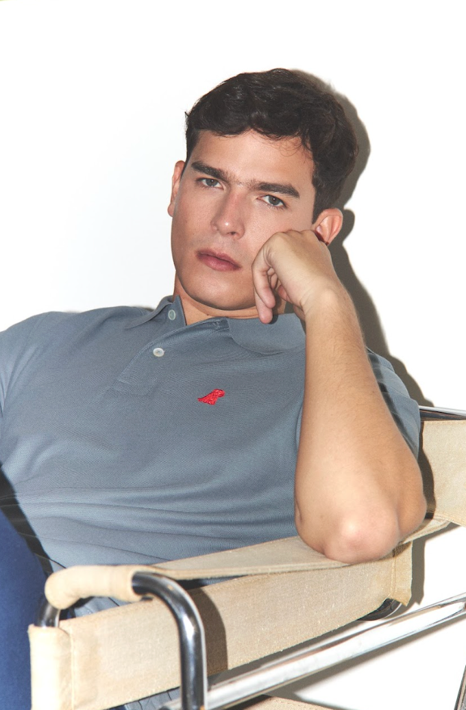 Un hombre joven con un polo gris está sentado en una silla de lona y cromo