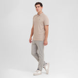 Man wearing a beige polo shirt and gray pants on a white background