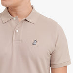 Close-up of a beige polo shirt with a small logo on a white background