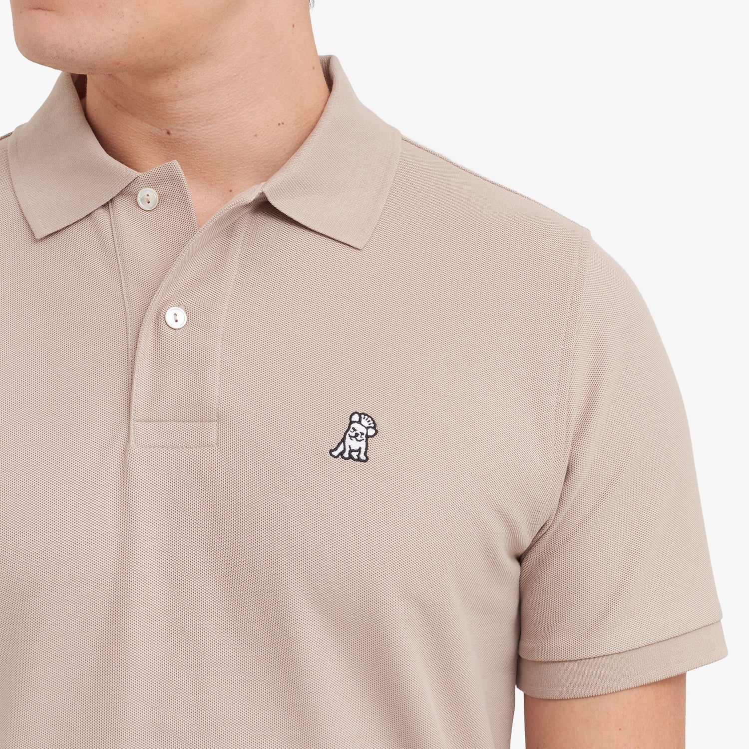 Close-up of a beige polo shirt with a small logo on a white background