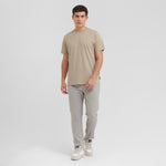 Man wearing a beige t-shirt and light gray pants on a white background