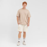 Man wearing a beige t-shirt and white shorts on a plain background