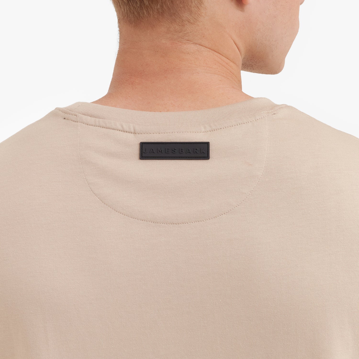 Close-up of a beige t-shirt with a brand label on the collar against a white background