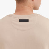 Close-up of a beige t-shirt with a brand label on the collar against a white background