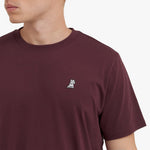 Close-up of a maroon t-shirt with a small white logo on a plain background