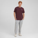 Man wearing a maroon t-shirt and gray sweatpants on a light gray background