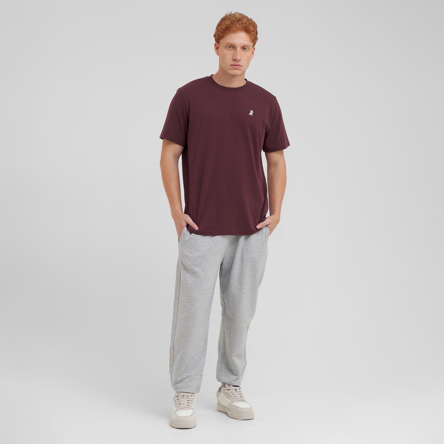 Man wearing a maroon t-shirt and gray sweatpants on a light gray background