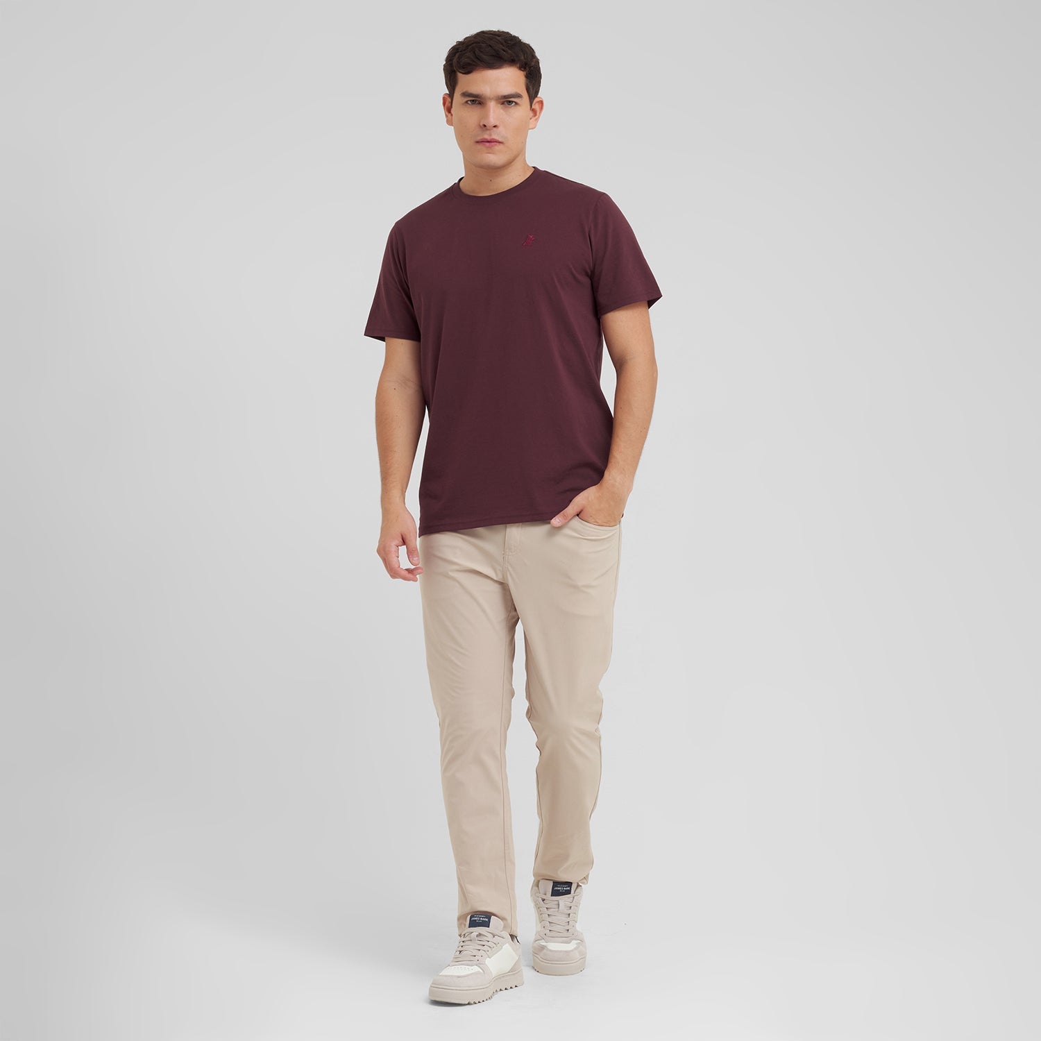 Man wearing a maroon t-shirt and beige pants on a white background