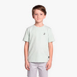 A boy wearing a light mint green T-shirt with a small black graphic on the left chest, paired with light gray shorts