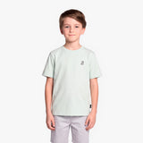 A boy wearing a light mint green T-shirt with a small black graphic on the left chest, paired with light gray shorts