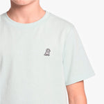 A close-up of a person wearing a pale mint green T-shirt with a small black dog on the left chest, set against a white background.