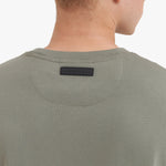 Close-up of a man wearing a green t-shirt with a brand label on the collar against a white background