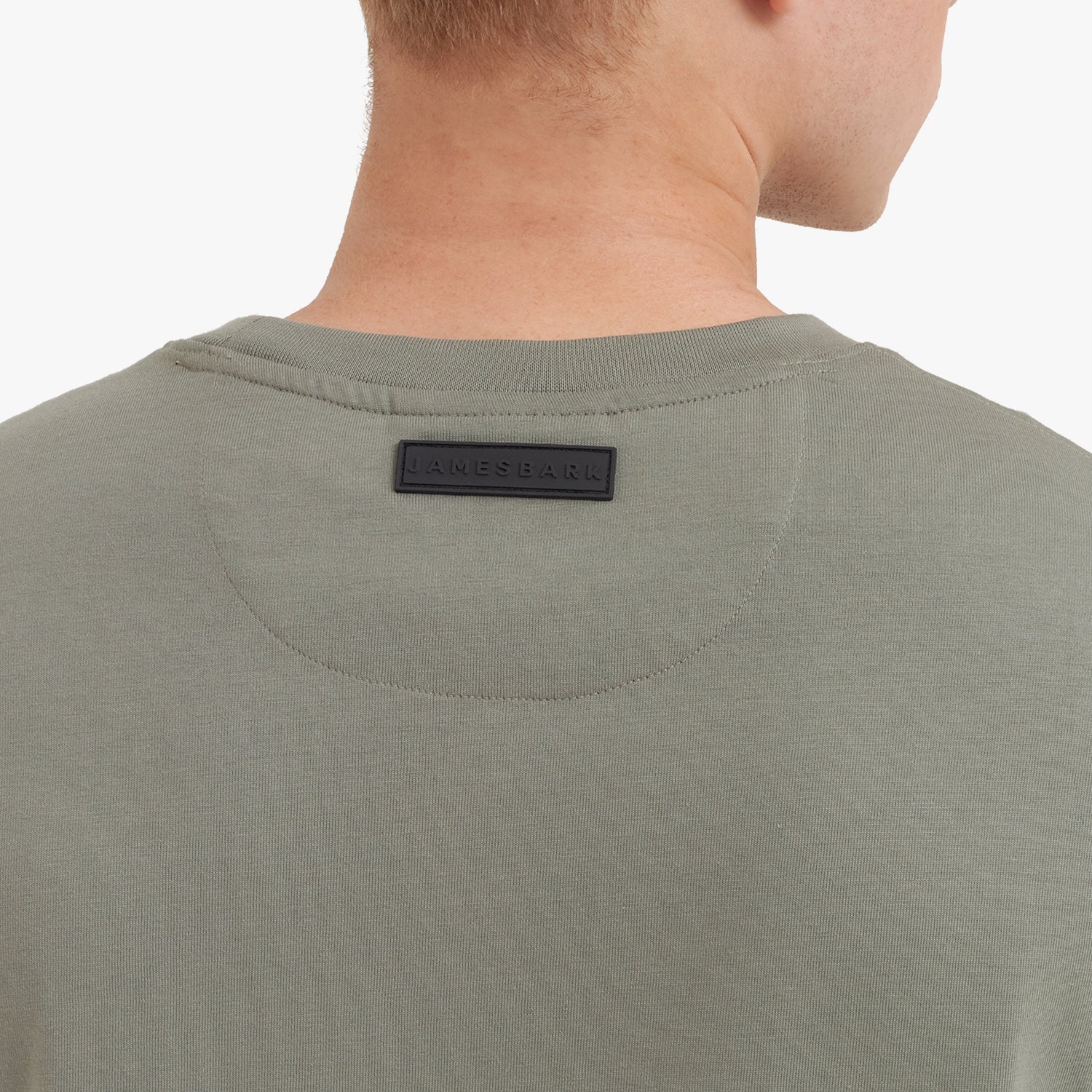 Close-up of a man wearing a green t-shirt with a brand label on the collar against a white background