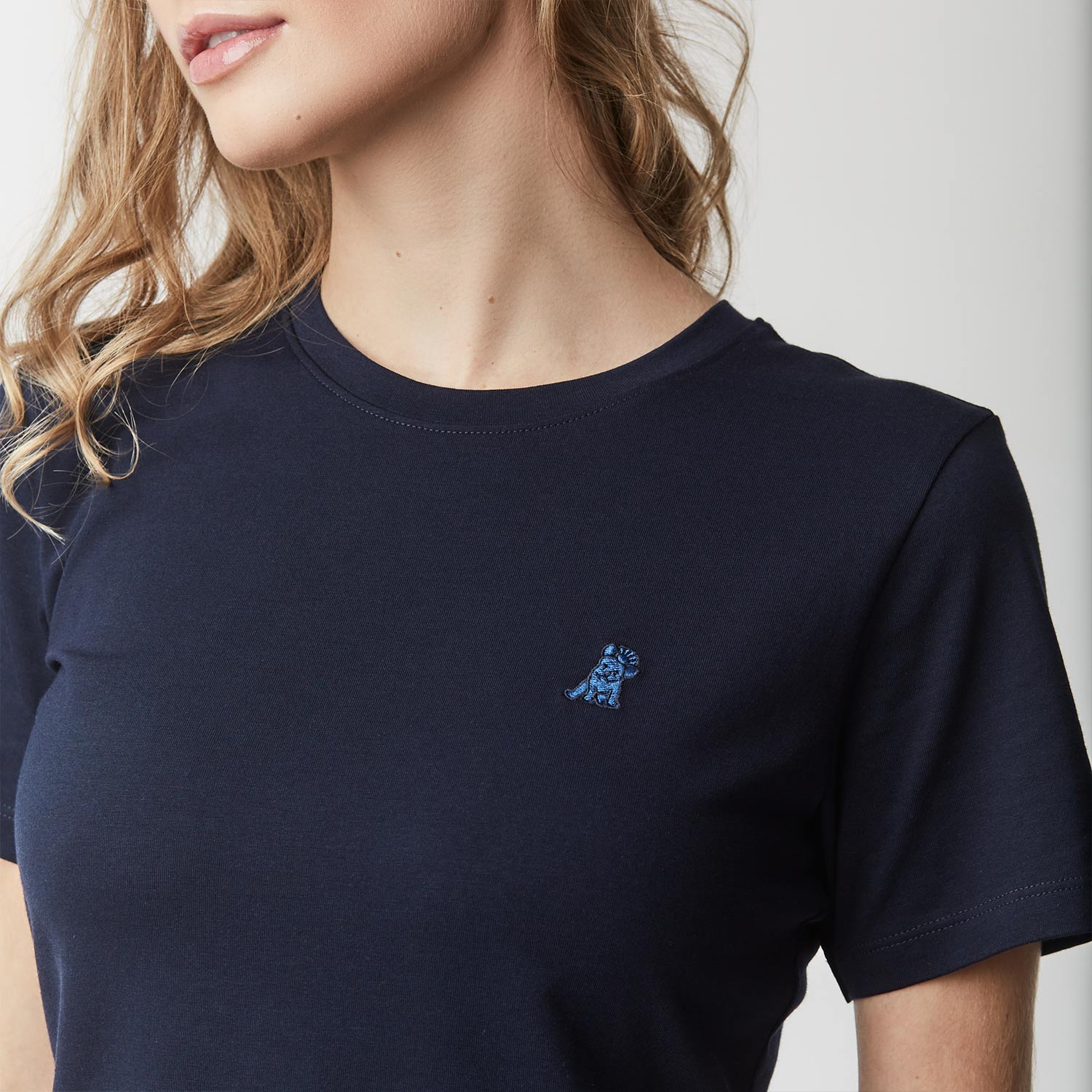 Close-up of the woman's upper body, highlighting the small embroidered logo on the chest of the navy blue t-shirt.
