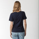 Rear view of a woman wearing the navy blue t-shirt and blue jeans.