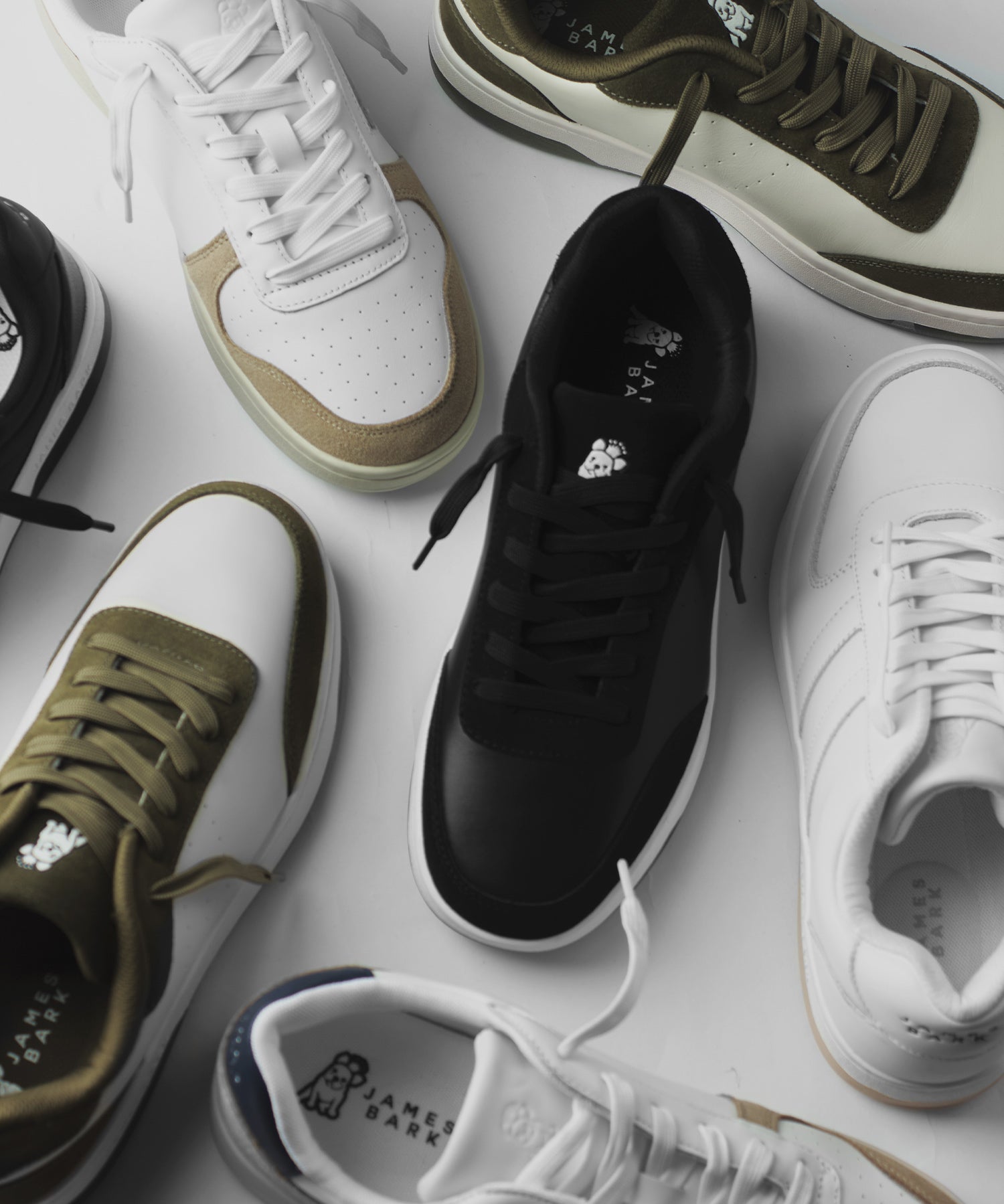Vista desde arriba de varios pares de zapatillas de deporte en colores blanco, negro y verde oliva, esparcidas sobre una superficie blanca